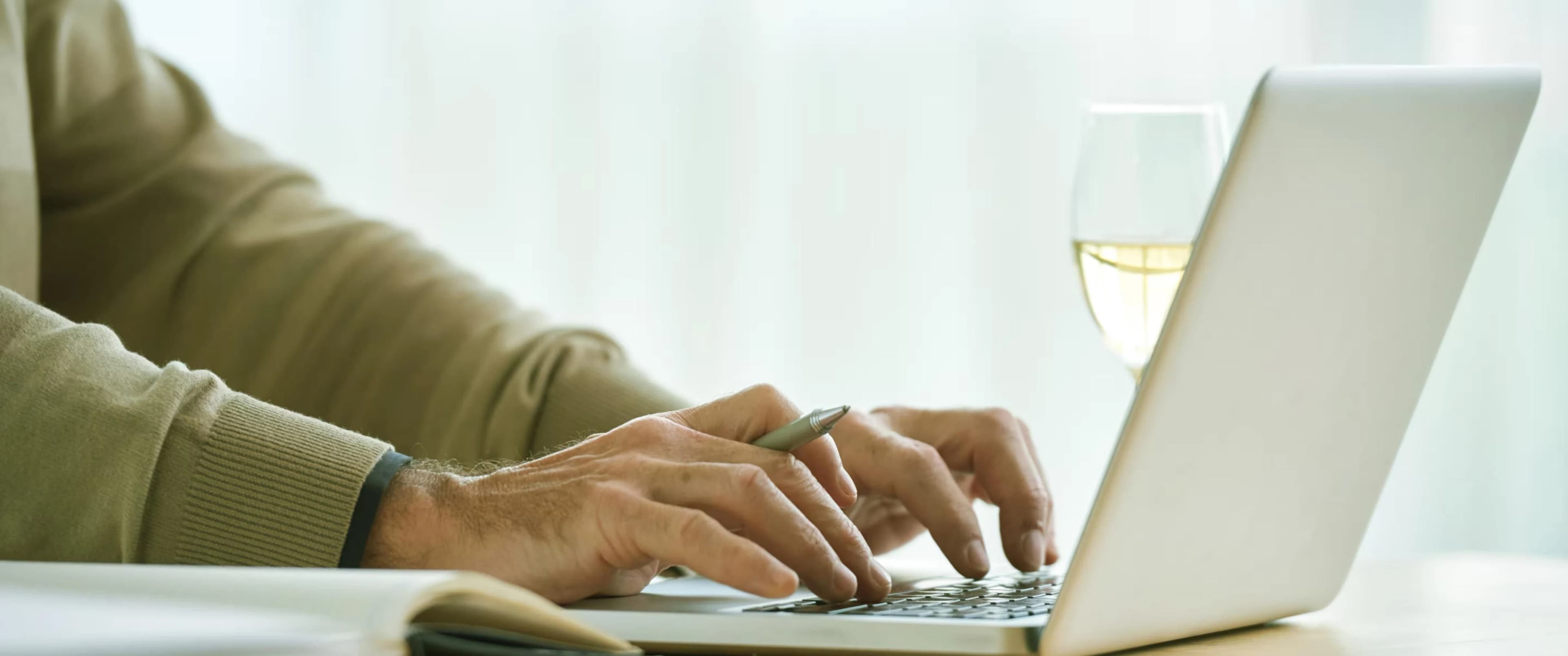 Mâini tastând la un laptop, cu un pix alături