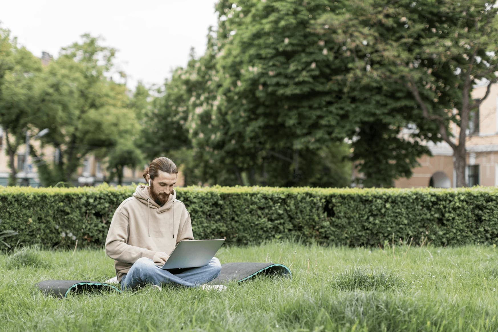 Bărbat așezat pe iarbă într-un parc, lucrând la laptop
